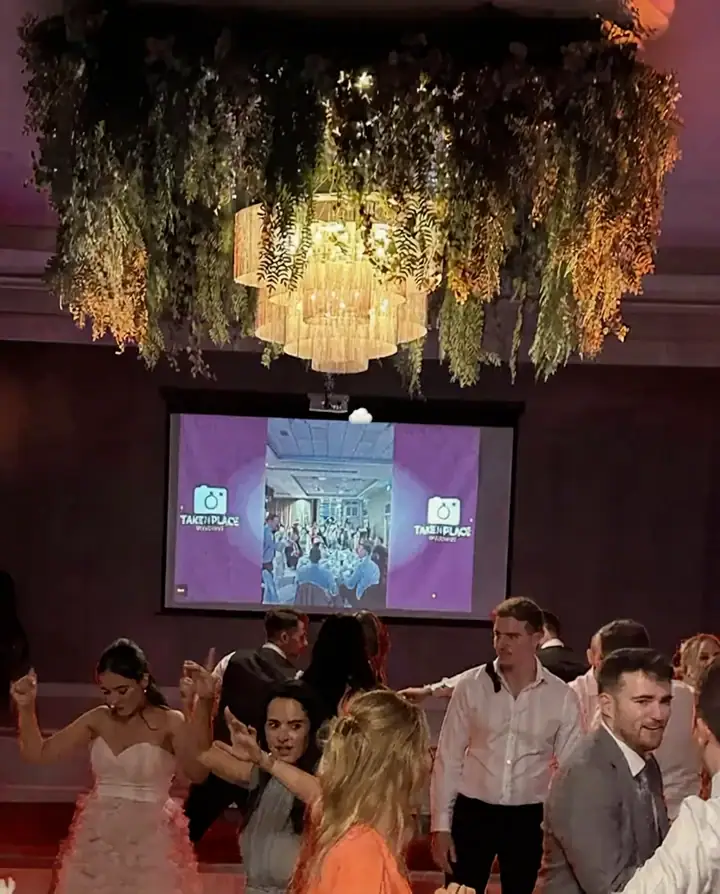 Wedding guests watching their own photos appear on the live takeNplace slideshow on the venue screen